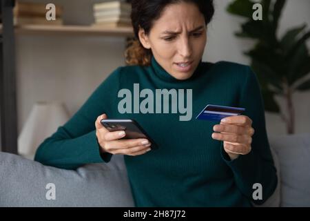 Scioccata giovane donna latina usando il telefono visto carta di banca rifiutata Foto Stock
