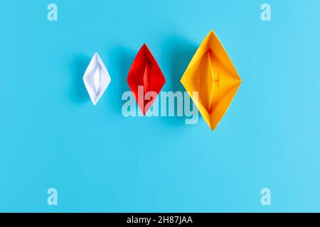 Tre barche di carta con dimensioni e colori diversi su sfondo blu. Concetto di diversità. Foto Stock