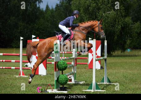 La giovane ragazza equestre salta ostacolo con cavallo di baia in show jumping Foto Stock