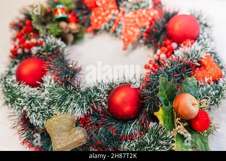 Corona di Natale di tinsel decorativo, bacche rosse di Natale e Natale albero festivo giocattoli sulla porta anteriore primo piano. Corona fatta a mano per la casa decorati Foto Stock