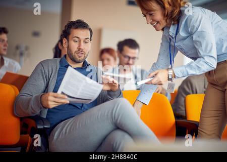 Un giovane partecipante di sesso maschile che chiede assistenza al docente in un'atmosfera rilassata durante la conferenza d'affari. Affari, persone, meeting, azienda Foto Stock