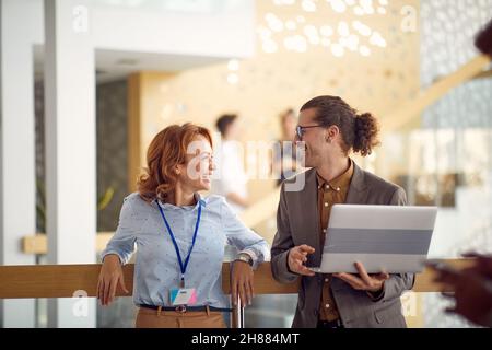 Una dirigente di affari femminile sta levandosi in piedi nel corridoio e sta avendo un buon tempo mentre chiacchiera in un'atmosfera amichevole con il suo collega maschio giovane. Autobus Foto Stock