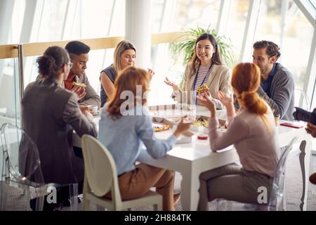 Gruppo di giovani uomini d'affari sta gustando una pausa pranzo al lavoro in un'atmosfera amichevole insieme. Aziende, persone, aziende Foto Stock