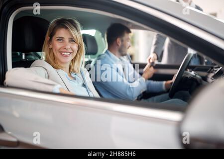 Famiglia felice in un'atmosfera eccitata seduta nella nuova macchina che hanno comprato in un negozio di auto. Auto, negozio, acquisto Foto Stock