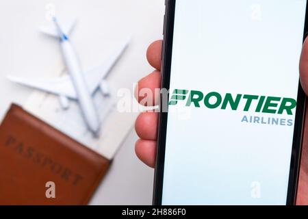 L'applicazione della compagnia aerea di Frontier Airlines viene visualizzata sullo schermo dello smartphone. Sullo sfondo c'è un aereo sfocato, un passaporto e una carta d'imbarco. Novembre 2021, San Francisco, USA Foto Stock