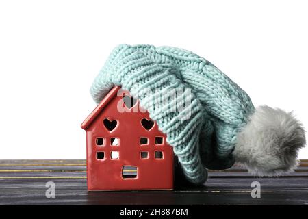 Casa giocattolo con cappello caldo sul tavolo su sfondo bianco. Concetto invernale Foto Stock