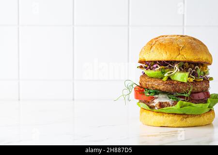 Hamburger vegano con avocado, salsa di pomodoro e arachidi, fondo bianco, spazio copia. Concetto di dieta a base di piante. Foto Stock