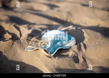 Inquinamento da maschera medica monouso sulla spiaggia da mare a causa coronavirus pandemia. Foto Stock