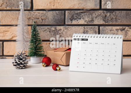 Calendario di carta per gennaio 2022 e decorazioni di Natale su tavola di legno bianco vicino muro di mattoni Foto Stock