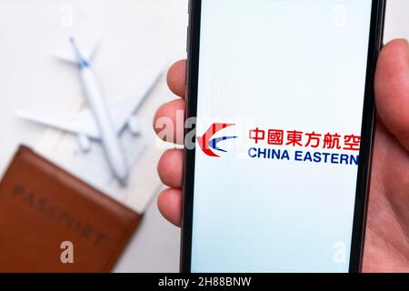 Logo dell'app China Eastern Airlines sullo schermo del telefono cellulare. Un'immagine sfocata di un aereo, un passaporto e una carta d'imbarco sullo sfondo. Novembre 2021, San Francisco, USA Foto Stock