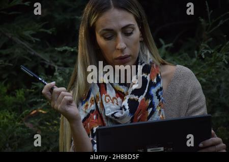 bella donna che lavora con un tablet all'aperto sull'erba in un parco, indossando abiti casual da hippster Foto Stock