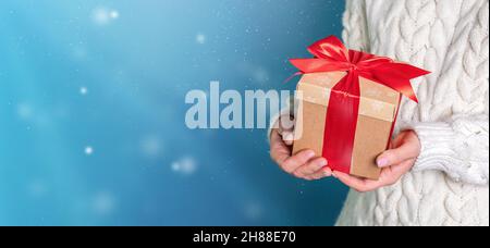 Nelle mani di un primo piano regalo di Natale, su sfondo blu con fiocchi di neve Foto Stock
