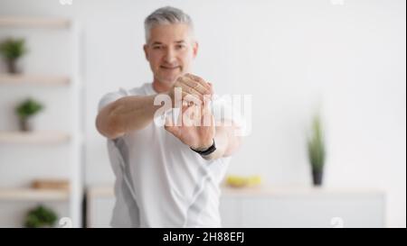 Uomo maturo che allunga le mani, esercitandosi, facendo esercizi di flessibilità, panorama con spazio libero, fuoco selettivo Foto Stock