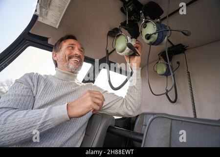 Uomo sorridente che prende le cuffie per l'aviazione prima di volare in elicottero Foto Stock