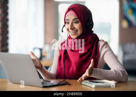 Allegra signora musulmana che ha video conferenza con i clienti Foto Stock