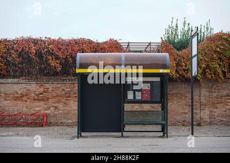 Fermata dell'autobus di fronte a un muro e cespugli. A sinistra, un cavalletto rosso per bicicletta. Foto Stock