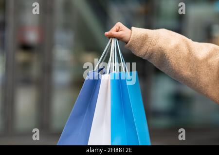 Vista croppata della giovane donna in inverno vestiti che tengono i sacchetti luminosi del regalo all'aperto, shopping per la stagione fredda, primo piano Foto Stock