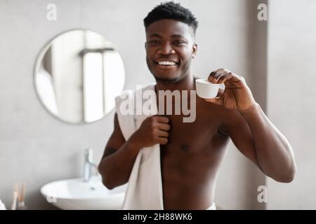 African American Male che mostra vaso crema viso posa in bagno Foto Stock