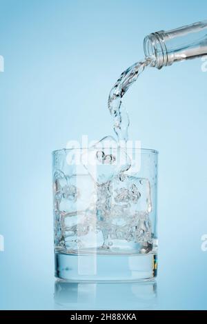 Bicchiere con acqua e cubetti di ghiaccio su sfondo blu Foto Stock