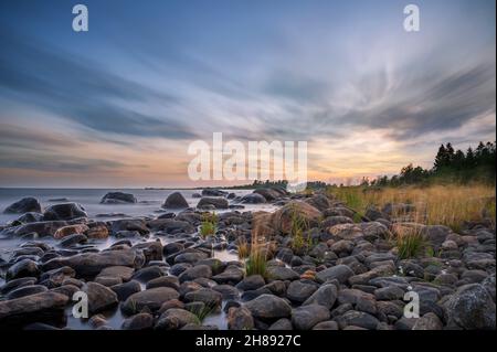 Lunga esposizione di un magnifico tramonto morbido e colorato vicino alla pietra del mare. Bel movimento nube con pietre di mare. Foto Stock