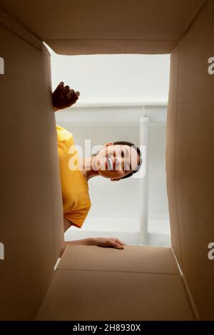 Eccitata signora asiatica guardando all'interno della scatola del pacco e sorridendo, ottenendo l'ordine in linea all'interno, soddisfatto con le merci consegnate Foto Stock