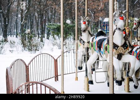 Giostra di cavalli con giostra nel parco invernale. Inverno neve paesaggio con retro giostra cavallo bianco. Fuori stagione inverno abbandonato divertimento Foto Stock