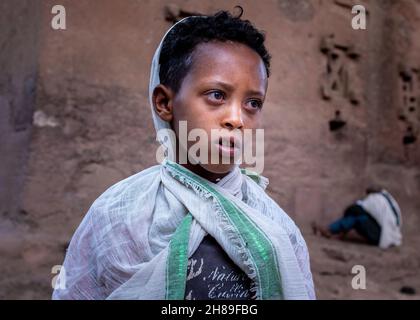 Lalibela, Etiopia - 23 maggio 2021: Ragazzo che elemosina fuori da una chiesa e indossa abiti bianchi sopra la sua maglietta Foto Stock