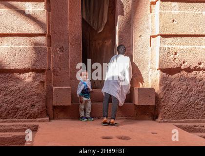 Lalibela, Etiopia - 23 maggio 2021: Due ragazzi che aspettano fuori da una chiesa, indossando abiti bianchi sopra i loro panni usuali Foto Stock