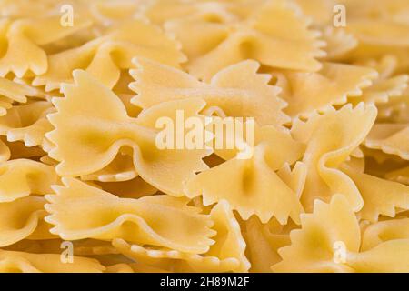 Dettaglio di pasta di farfalla di uovo crudo su mucchio con bella sfocatura sullo sfondo. Pasta con bow-tie gialla. Farfalle secche non cotte, bordo smerlato. Foto Stock