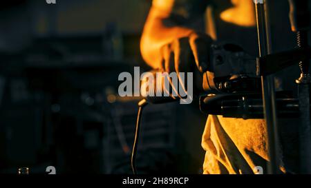 Primo piano del pezzo di ferro lucidato da un operatore di fabbrica. Riprese in stock. Il lavoratore con le mani sporche lucida la parte di ferro con la levigatrice a mano su sfondo scuro. Scintille Foto Stock