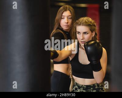 Allenamento fitness boxe femminile in palestra. Lo sportivo biondo, sotto la guida di un allenatore, esegue colpi su un sacco di punzonatura. Foto Stock