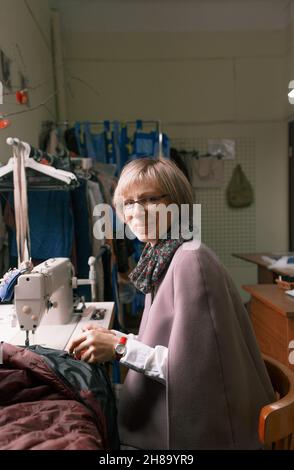 Una donna dressmaker utilizza una macchina da cucire per creare abiti personalizzati in un'officina. Una sartstress femminile è occupato cucire abiti sul posto di lavoro. Foto Stock