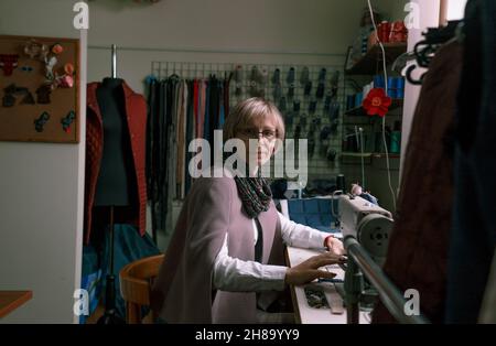 Una donna dressmaker utilizza una macchina da cucire per creare abiti personalizzati in un'officina. Una sartstress femminile è occupato cucire abiti sul posto di lavoro. Foto Stock