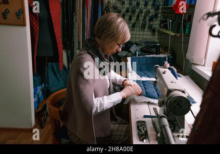 Una donna dressmaker utilizza una macchina da cucire per creare abiti personalizzati in un'officina. Una sartstress femminile è occupato cucire abiti sul posto di lavoro. Foto Stock