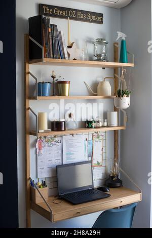Piccola stazione remota per uffici domestici, area di lavoro, con computer portatile, piante domestiche, scheda metallica, candele e lampada da tavolo. Scatto verticale. Foto Stock