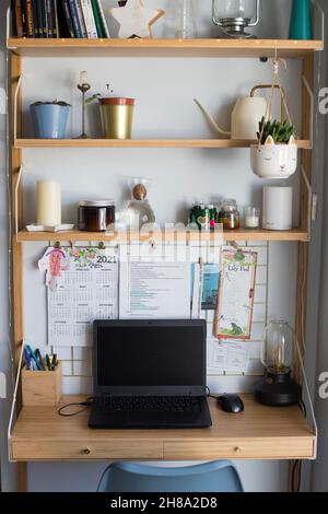 Piccola stazione remota per uffici domestici, area di lavoro, con computer portatile, piante domestiche, scheda metallica, candele e lampada da tavolo. Scatto verticale. Vista frontale. Foto Stock