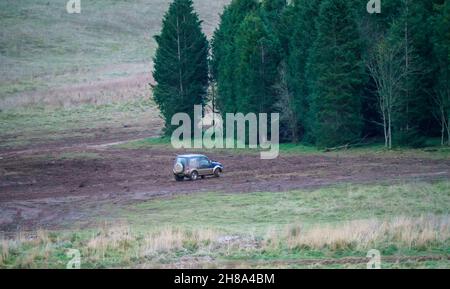 Blu e argento Suzuki Jimny 4x4 fuoristrada guidato intorno a una distesa fangosa nel bosco, Wiltshire UK Foto Stock