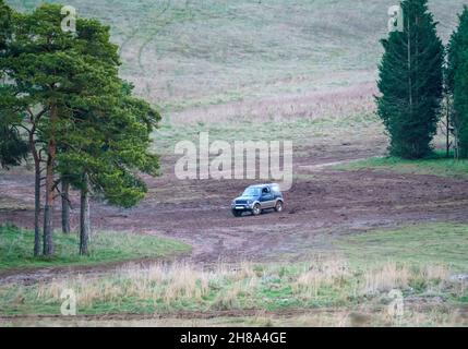 Blu e argento Suzuki Jimny 4x4 fuoristrada guidato intorno a una distesa fangosa nel bosco, Wiltshire UK Foto Stock