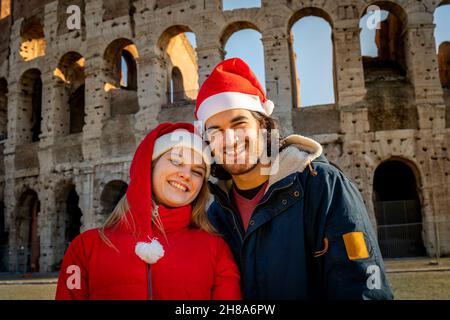 Una bella giovane coppia che fotografa di fronte al Colosseo con i cappelli rossi di Santa. Sensazione di felicità e amore. Vacanza di Natale concetto. Foto Stock