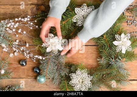 Donna che decora la corona di Natale fatta di rami di abete su sfondo di legno Foto Stock