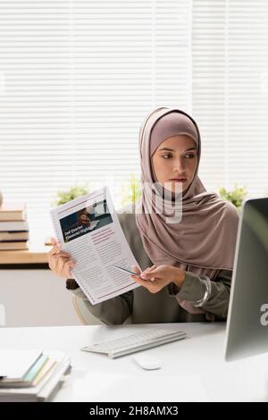 Giovane insegnante musulmana nel hijab che punta al documento finanziario mentre fa la presentazione durante la lezione in linea Foto Stock