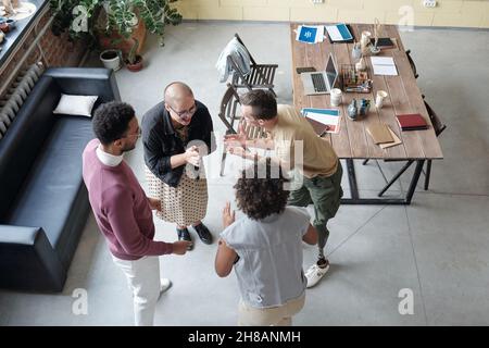 Molti giovani impiegati felici che si divertono a rottura mentre si levano in piedi in cerchio tra il divano di pelle nera ed il tavolo e giocano Foto Stock