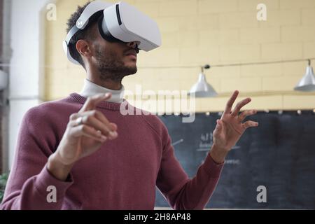 Giovane uomo d'affari contemporaneo in cuffie per realtà virtuale che si prepara o guarda attraverso la presentazione online Foto Stock