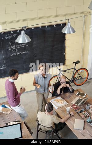 Giovani dirigenti d'ufficio contemporanei che interagiscono alla pausa pranzo mentre si ha pizza dal posto di lavoro Foto Stock