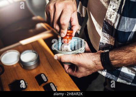 Barbiere nel barbiere preparazione della schiuma da barba in una ciotola con una spazzola. Foto Stock