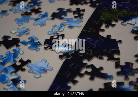 I pezzi centrali blu e bianchi profondi di un puzzle incompiuto sono sparsi su un tavolo vicino al bordo finito. Foto Stock
