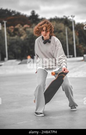 Ragazza sulle gambe piegate che tocca lo skateboard con la mano Foto Stock