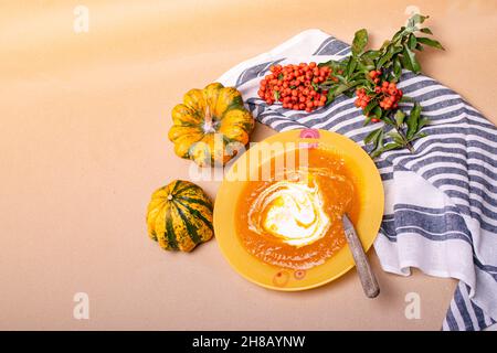 Zuppa di zucca in un piatto, accanto alle foglie di piatto, zucchine, asciugamano da cucina. Foto Stock