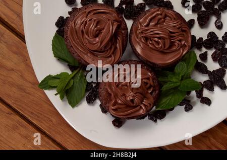 Deliziose frittelle con glassa di cioccolato, uvetta e foglie di menta su un piatto bianco su un tavolo di legno. Dessert fatto in casa Foto Stock