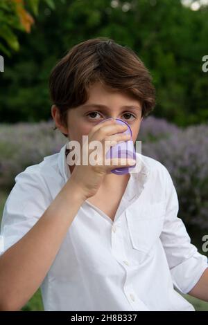 Ritratto di ragazzo che beve da tazza in campo di lavanda Foto Stock